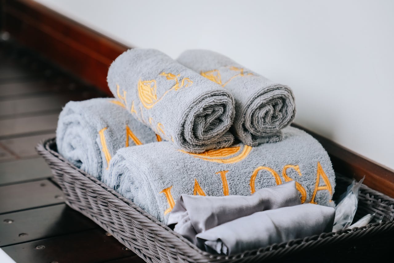 Close-up of neatly rolled gray towels with golden embroidery in a stylish wicker basket.